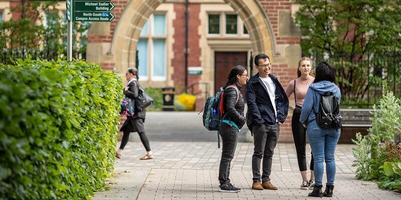A busy campus with two prospective students chatting to an open day ambassador