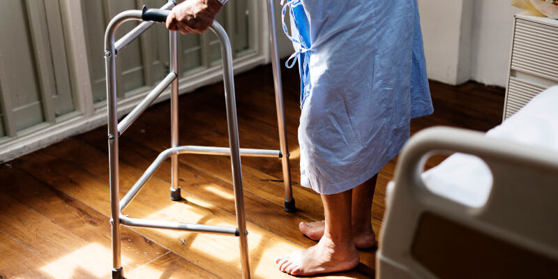 An elderly person in a hospital gown using a walking frame