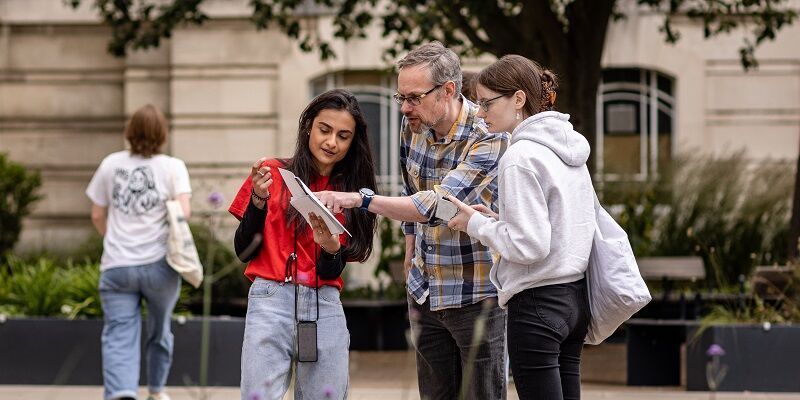 A student and their parent or guardian talking to a student ambassador on campus who is pointing to a document