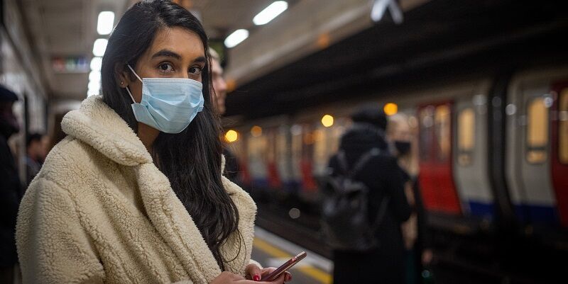 Person wearing a mask, on an Underground platform, waiting for a train