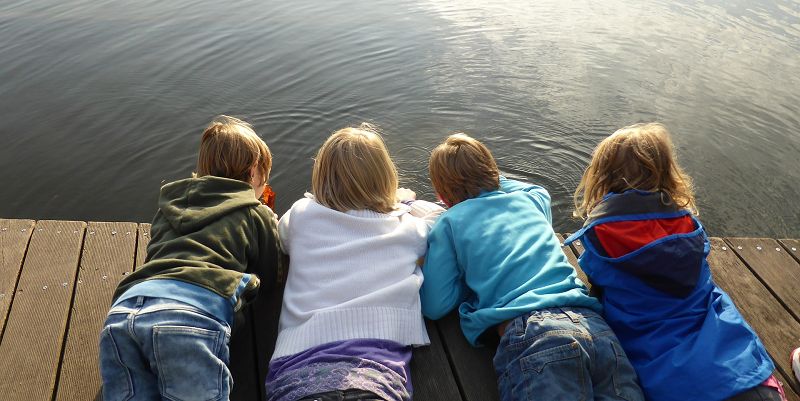Four children lying on wooden decking looking into a river. They all have their backs to the camera.